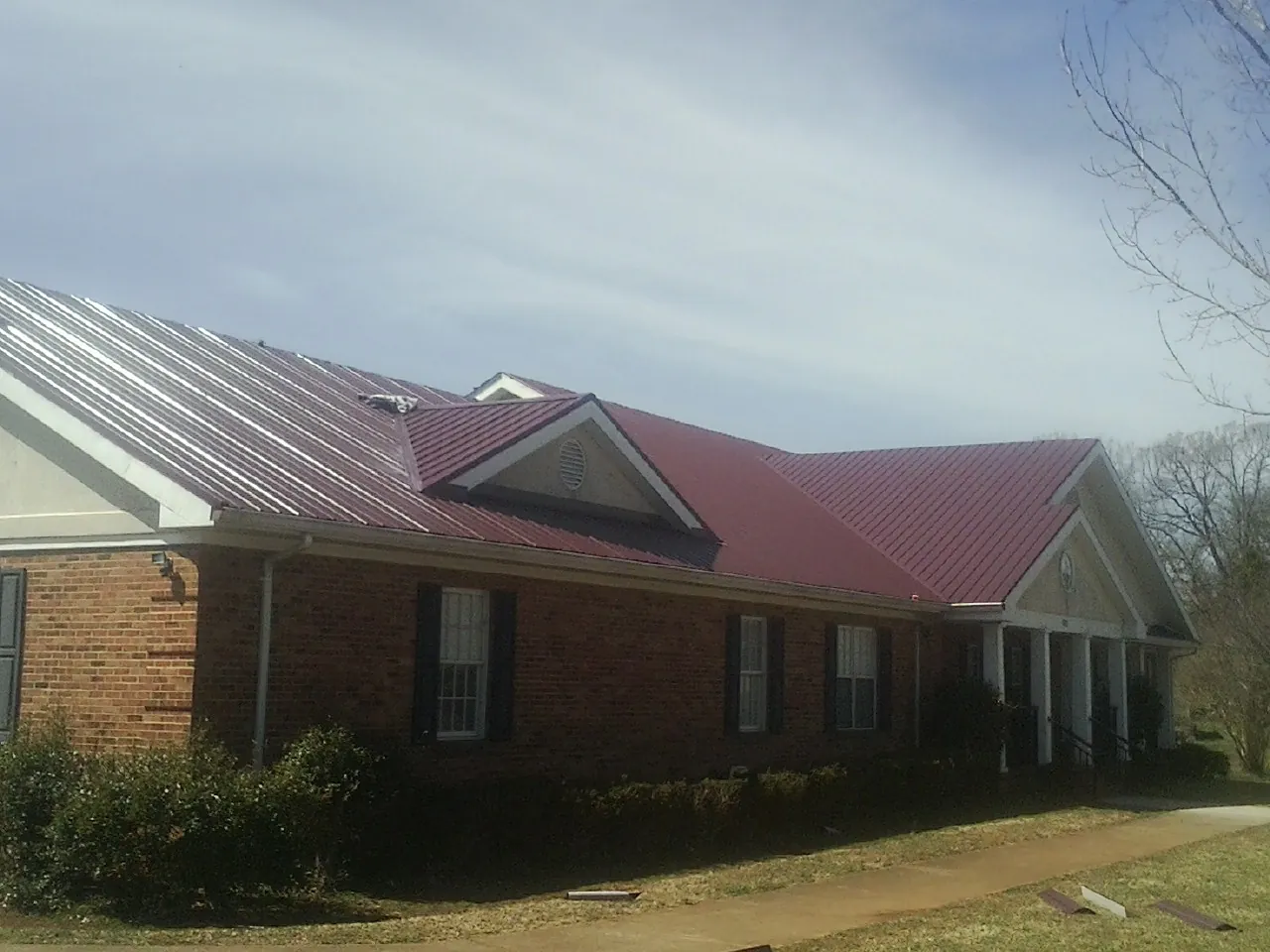 Red metal roof with gabled entries on a long brick building, from a Hail Damage Roof Repair job in Pink Hill
