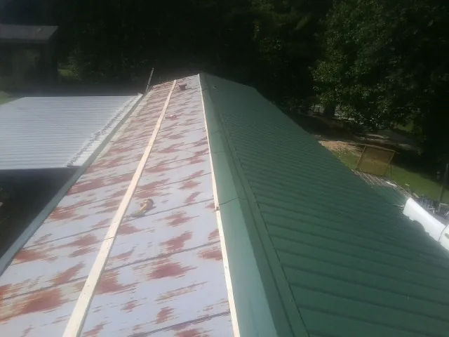 Old rusted panels beside newly installed green metal roofing — Wind Damage Roof Repair by Roofing Brothers in Pink Hill