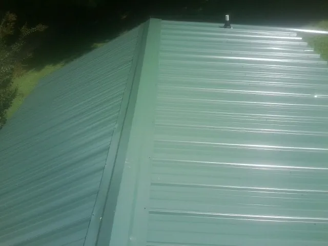 New green metal panels meeting at the ridge of a roof — Flat Roof Repair work by our crew in Pink Hill
