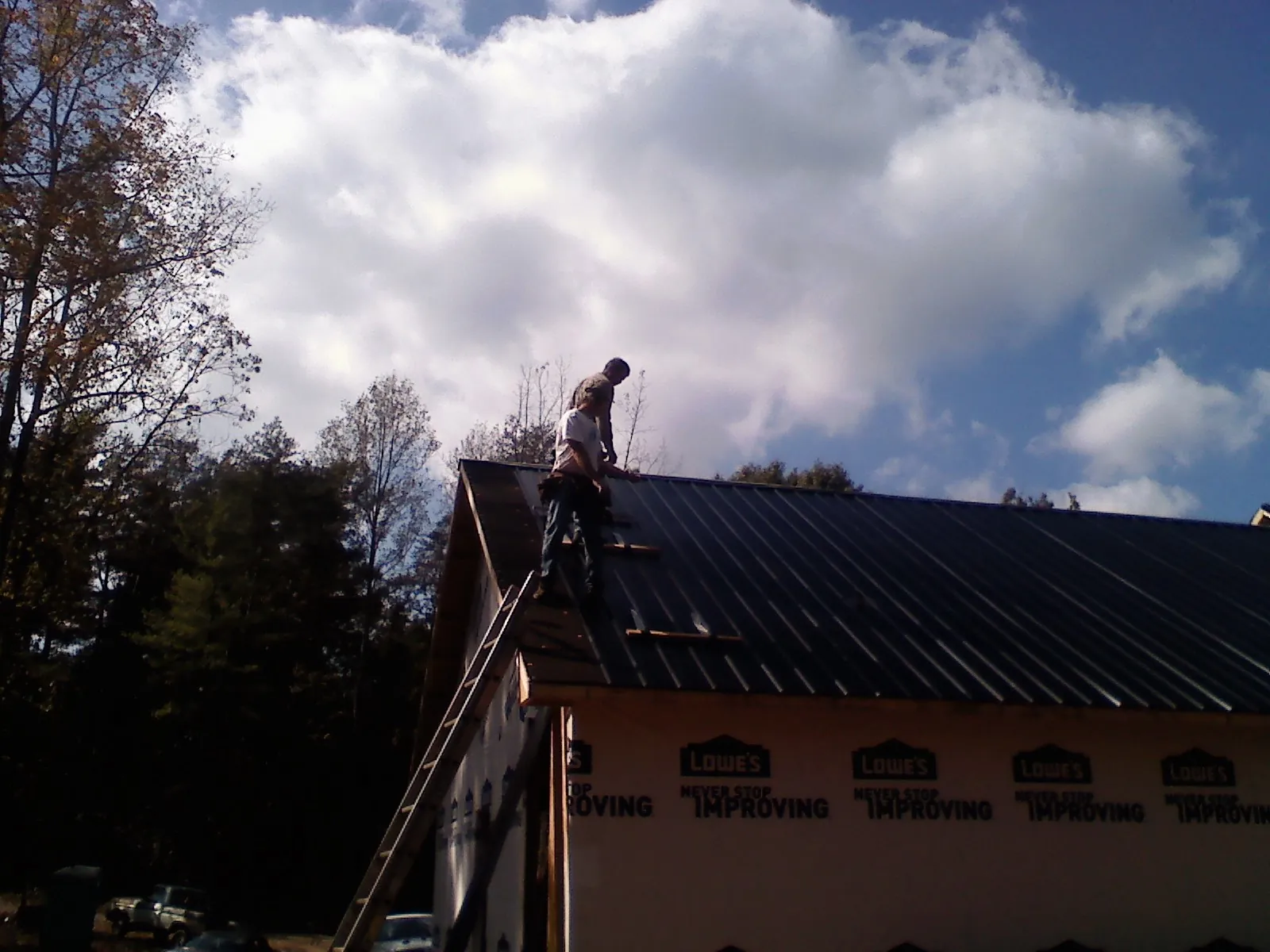 Roofer fastening dark metal panels high against a cloudy sky, from a Roof Inspection job in Pink Hill