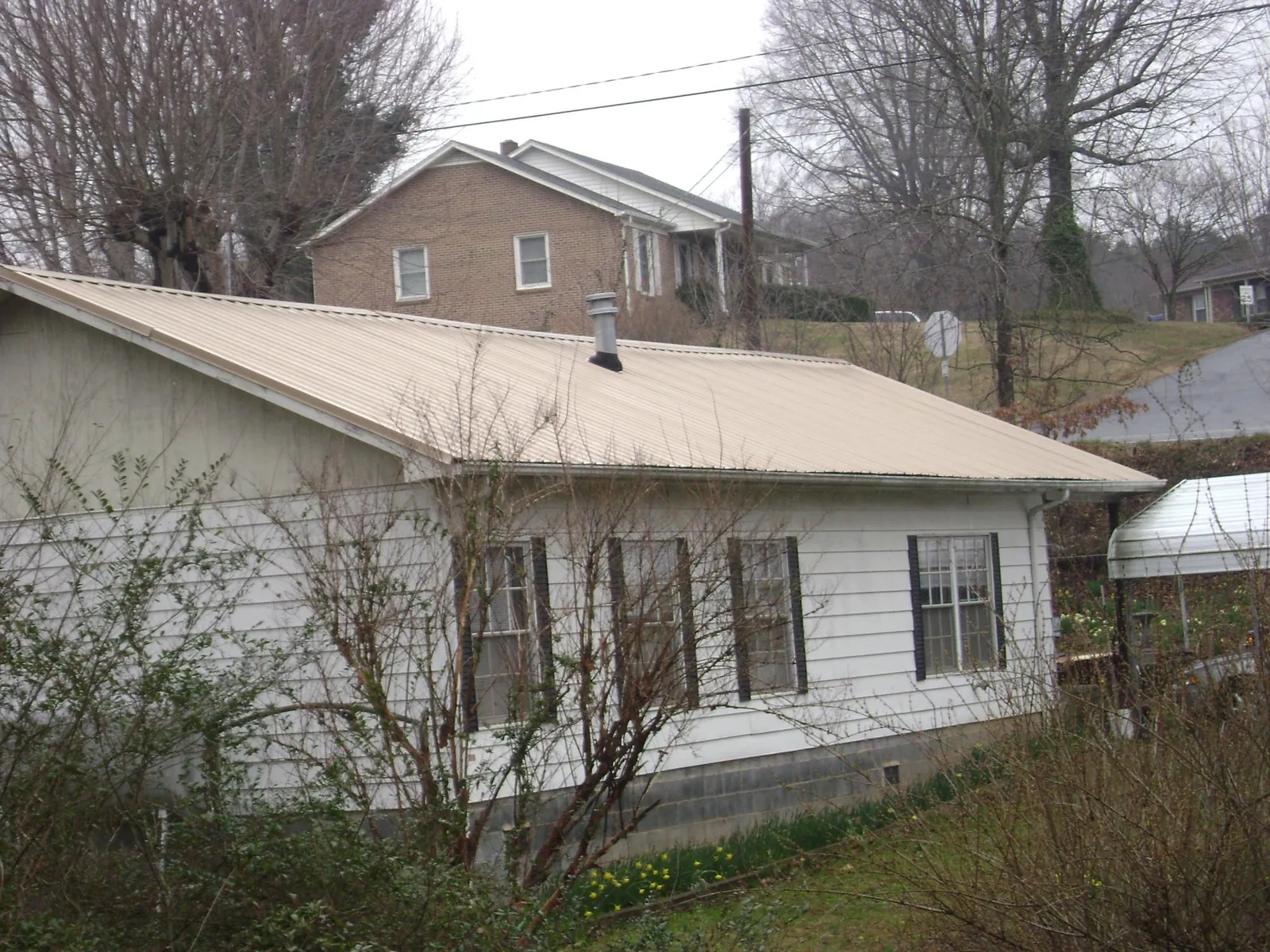 Tan metal roof on a white sided house set into a hillside — Commercial Roofing by Roofing Brothers in Pink Hill